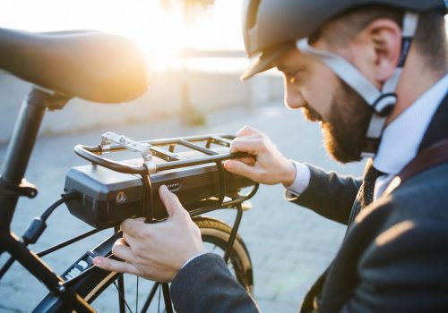 Hipster businessman commuter setting up electric bicycle in city. Hipster businessman commuter setting up electric bicycle when traveling home from work in city.