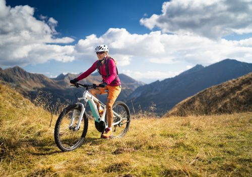 happy woman on electric mountain bike high up in european mountains smiling fit sporty woman cycling her electric mountain bike high up in mountains on sunny autumn day with white clouds